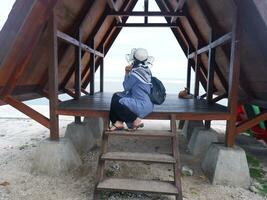 Back of the woman in the hat on the tropical beach who is sitting in the gazebo looking up at the sky and the sea photo