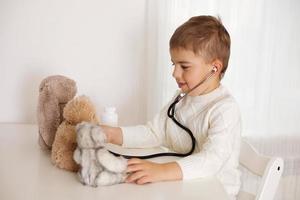 Cute little boy playing doctor at home and curing plush toy. Sweet toddler child using stethoscope. Having fun. Kids and medicine, healthcare. photo