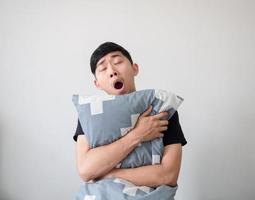 Asian young man wake up and hugging pillow yawn and feel sleepy on white isolated,Lazy concept photo