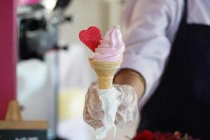 A worker with gloves holding an ice cream cone with a mix flavours pink and vanilla. pink ice cream with a red heart. photo