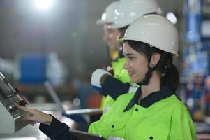 joven ingeniera aprendiendo a operar maquinaria en una fábrica con ingenieros veteranos foto