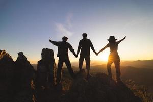 silhuette grupo joven rezando en la montaña, brazos extendidos observando un hermoso amanecer dramático. foto