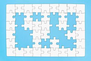 Unfinished white jigsaw puzzle on blue background with copy space. Business strategy teamwork and problem solving concept. photo