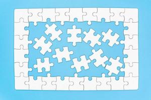 Unfinished white jigsaw puzzle on blue background with copy space. Business strategy teamwork and problem solving concept. photo