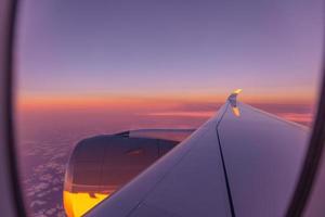 hermosa vista panorámica del amanecer al atardecer a través de la ventana del avión con alas. mirando por la ventana, concepto de fondo de viaje, ventana de avión con rayos de sol. plantilla de aviación perfecta foto