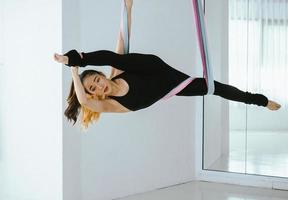 joven y bella bailarina asiática vestida de negro realizando danza aérea con telas multicolores en el estudio. foto