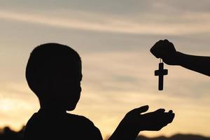silueta de un hombre rezando con una cruz en la mano al amanecer, concepto de religión. foto