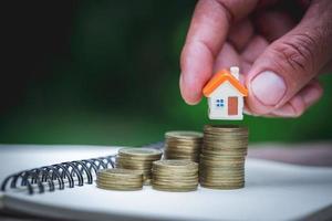 Woman's hand putting house model on coins stack. Concept for property ladder, planning savings money of coins to buy a home concept property mortgage and investment for a house. photo