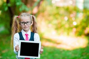 Adorable little girl holding tablet PC outdoors in autumn sunny day photo