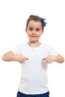 Positive little girl in casual white t shirt indicates at blank space for logo design