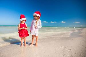 vista trasera de niñas lindas con sombreros de navidad en la playa exótica foto