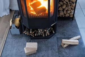 Fuel briquettes made of pressed sawdust for kindling the furnace - economical alternative eco-friendly fuel for the fireplace in the house. Firewood is burning in the oven in the interior photo