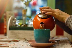 mujer de primer plano en un café vierte té, tetera y taza de té. foto