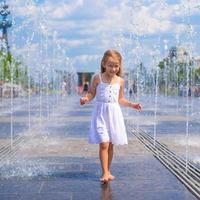 Cute girl having fun in outdoor fountain at hot day photo