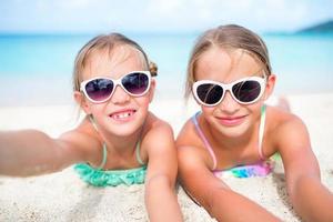 Little girls having fun at tropical beach playing together at shallow water. Adorable little sisters at beach during summer vacation photo