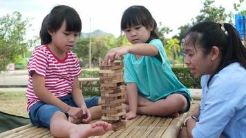 niños emocionados y mamá jugando al juego de bloques de madera de la torre jenga juntos en el parque. familia feliz con niños disfrutando juntos de las actividades de fin de semana. video