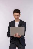 Portrait of young handsome smiling businessman holding laptop in hands, typing and browsing web pages isolated on white background photo