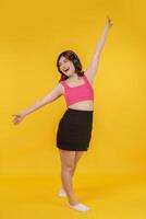 Portrait of Happy young woman listening music in headphones and singing while standing isolated over yellow background photo