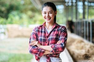 Portrait of Happy young Asian farmer woman crossing arm and looking at camera at dairy cow farm. Agriculture industry, farming, people, technology and animal husbandry concept. photo