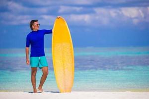 Happy young surf man at white beach with yellow surfboard photo