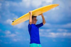 Happy young surf man at white beach with yellow surfboard photo