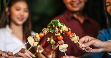 Happy Asian friends cheering with barbecue dinner outdoor - Group of people having fun in new year party. People, food and drink lifestyle concept Night Party, people and celebration concept. photo