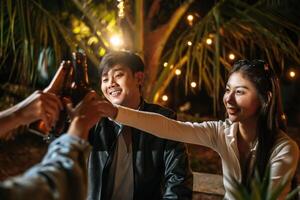 Portrait of Happy Asian friends having dinner party together - Young people sitting at bar table toasting beer glasses dinner outdoor  - People, food, drink lifestyle, new year celebration concept. photo