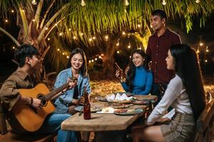 retrato de feliz grupo asiático de amigos divirtiéndose con música cenando y bebiendo juntos al aire libre - grupo de amigos felices brindando cervezas - gente, comida, estilo de vida de bebida, concepto de celebración de año nuevo. foto