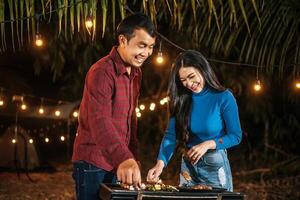 Happy Asian couple cheering with barbecue dinner outdoor - Group of people having fun in new year party. People, food and drink lifestyle concept Night Party, people and celebration concept. photo