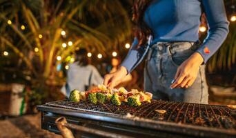 Close up hand of Woman cooking meat on barbecue grill at new year party. Bar-B-Q or BBQ on traditional stove. Night Party, people and celebration concept. photo