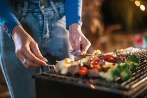 Close up hand of Woman cooking meat on barbecue grill at new year party. Bar-B-Q or BBQ on traditional stove. Night Party, people and celebration concept. photo