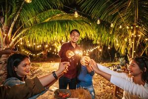 retrato de feliz grupo asiático de amigos divirtiéndose con bengalas al aire libre - jóvenes divirtiéndose con fuegos artificiales en la noche - gente, comida, estilo de vida de bebida, concepto de celebración de año nuevo. foto