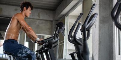 Topless athletic man cardio riding on bicycle at gym fitness photo
