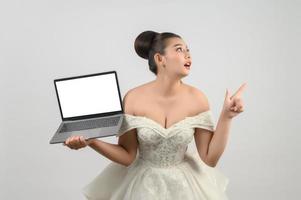 Young asian beautiful bride pose with mockup laptop computer in hand photo