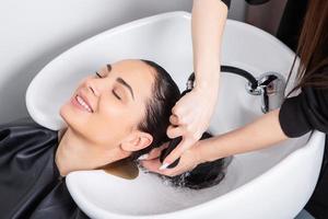 peluquero profesional lavando el cabello de una mujer joven en un salón de belleza foto