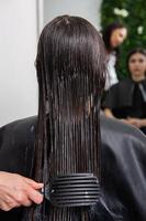 el peluquero aplica una máscara para el cabello al cabello negro liso. cuidado del cabello en el salón de belleza. foto