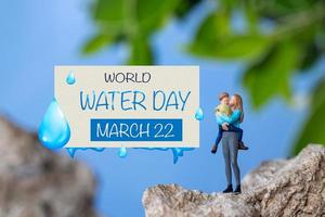 Miniature people mother holding son in the arms and words written on paper World Water Day photo
