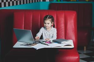 linda niña usando laptop en casa. concepto de regreso a la escuela. la niña hace su tarea sola en la computadora portátil foto