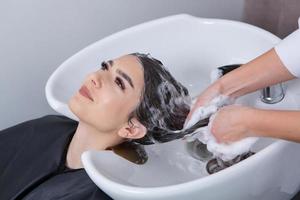 peluquero profesional lavando el cabello de una mujer joven en un salón de belleza. primer plano del cabello de la mujer en el salón de belleza, concepto de peinado foto