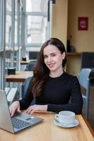 Beautiful businesswoman working on laptop in coffee shop. Female freelancer connecting to internet via computer. Blogger or journalist writing new article. photo