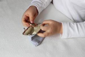 las manos de los niños ponen monedas en una billetera, una niña pequeña con dinero y pusre en la mano. aprender responsabilidad financiera y planificar ahorros. educación financiera para niños, apoyo financiero. invertir en niños foto