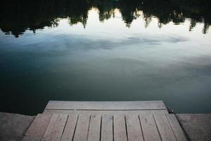 Close up wooden lake dock in front of woods reflecting in water concept photo