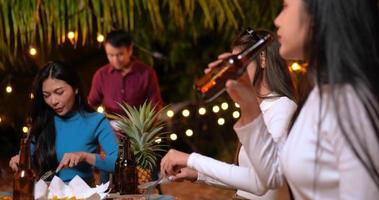 imágenes de amigos asiáticos felices cenando juntos - jóvenes sentados en la mesa del bar brindando una cena con botellas de cerveza al aire libre - gente, comida, estilo de vida de bebida, concepto de celebración de año nuevo. video