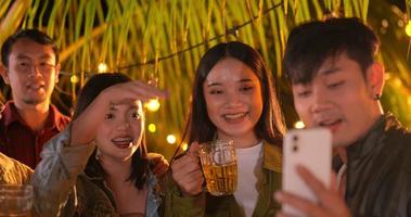 Footage of Happy Asian friends having dinner and selfie party together - Young people toasting beer glasses dinner outdoor  - People, food, drink lifestyle, new year celebration concept.