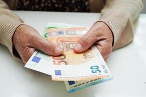 Retired elderly woman holding Euro banknotes money and worry about monthly expenses and treatment fee payment. photo