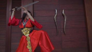 eine asiatische Frau, die vor dem Kampf in der Arena mit ihrem Schwert trainiert, während sie ein rotes Kleid trägt video