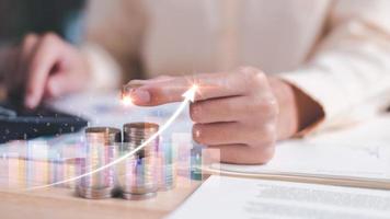 Human hand holding a coin ,pile of coins on table,profit growth graph,progressive ideas for improving financial and investment results,Interest rate data analysis, balance sheet, net profit account photo