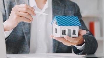 agente de corretaje de bienes raíces entrega una muestra de una casa modelo al cliente, contrato de préstamo hipotecario que arrienda y compra y vende casa y contrata el concepto de préstamo hipotecario de seguro de hogar