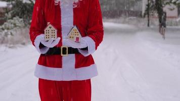 huissleutel met sleutelhanger huisje in handen van de kerstman buiten in de sneeuw. deal voor onroerend goed, aankoop, bouw, verhuizing, hypotheek. gezellig huis. vrolijk kerstfeest, nieuwjaarsboekingsevenement en hal video