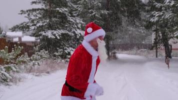 le père noël s'amuse et danse drôle, montre des tours acrobatiques, des éléments de combat et des sauts amusants en plein air en hiver sur une route enneigée avec des pins. célébrer noël et le nouvel an. video